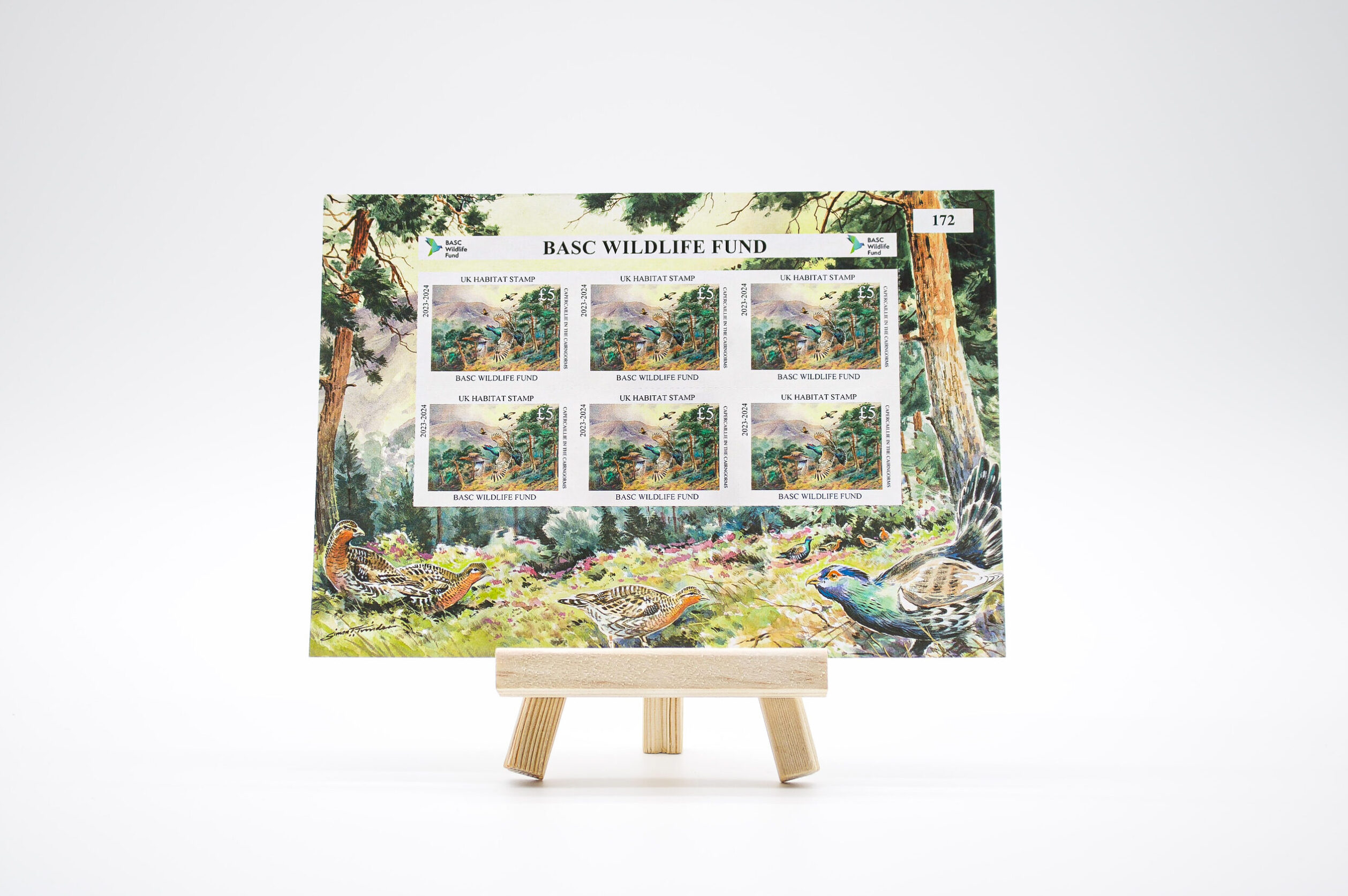 BASC Wildlife Fund 2023–2024 UK Habitat Stamp sheet on a wooden easel, showing six £5 stamps with capercaillie in flight over woodland in the Cairngorms, artwork by Simon Trinder.